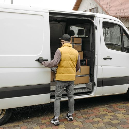 A delivery driver loads packages into a white van on a residential street.